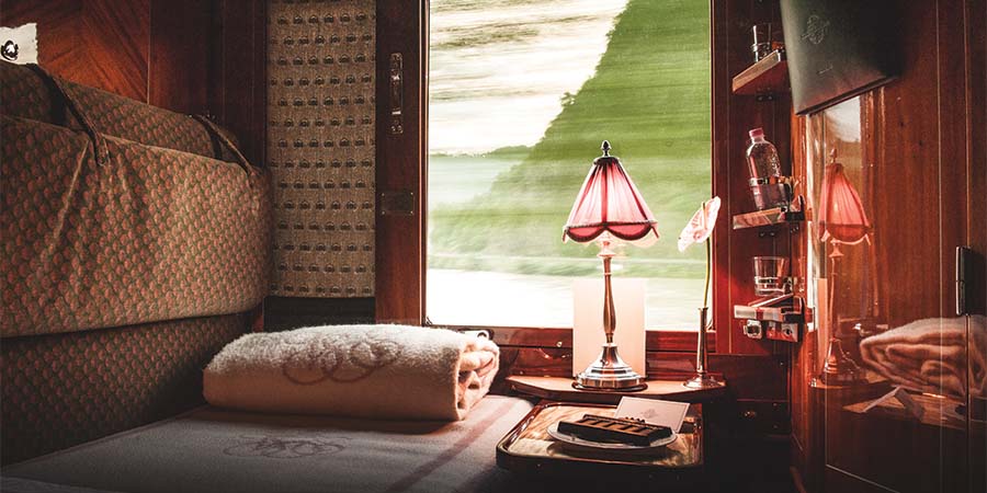Historic Cabin aboard the Venice Simplon Orient Express, featuring a folded blanket and lamp in front of a large window. 
